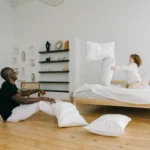 Child and adult enjoying a fun pillow fight in a stylish minimalist bedroom setting.