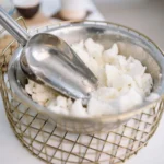 Close-up of a stainless steel bowl filled with candle wax and a scooper, suitable for candle making.