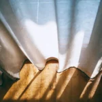 From above of panoramic window with transparent curtains lightened by sunshine in room