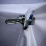 Close-up of a metal clamp holding white fabric, displaying industrial design.