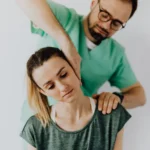 Concentrated doctor massage therapist in medical uniform doing therapeutic neck massage for calm young female patient in casual wear